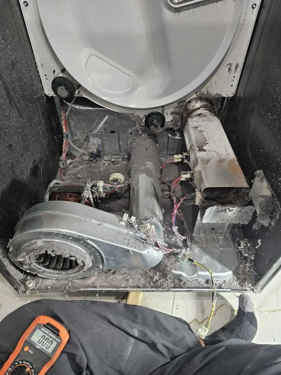 Inside view of a clothes dryer with the front panel removed, showing the drum, heating-element housing, thermal fuse, and dust accumulated on internal components — typical disassembly state during a no-heat diagnostic